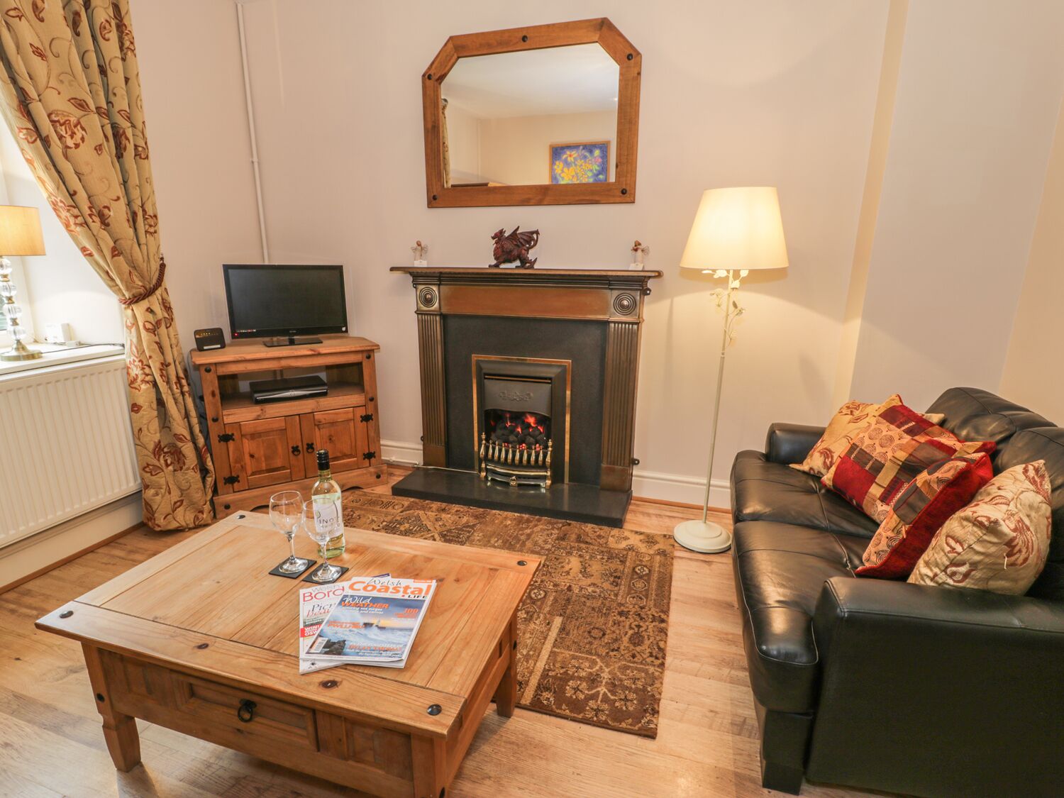Un salon avec une cheminée, un téléviseur, une table basse avec un magazine, un canapé avec des coussins et un lampadaire.