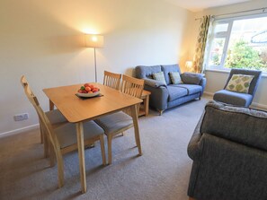 A living room with a wooden dining table, two wooden chairs, a blue sofa, and a grey armchair. - Fairfell (Keswick)