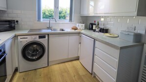 A compact kitchen with a washing machine, a sink, and a window with curtains. - Fairfell (Keswick)