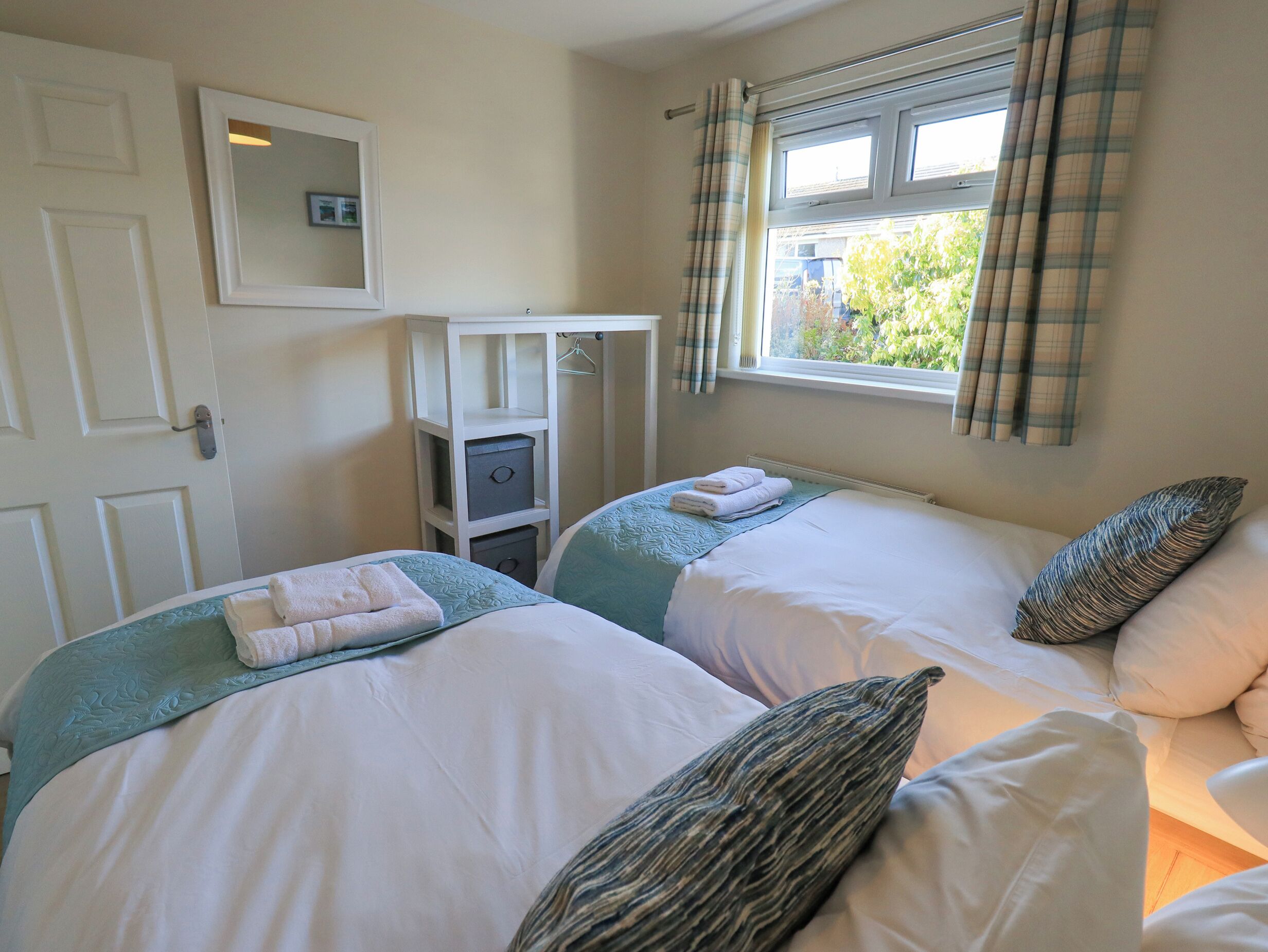 A bedroom with two beds, a wardrobe, a mirror, and a window with curtains.