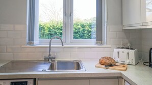 A kitchen with a double window, a stainless steel sink, a toaster, and a loaf of bread on a cutting board. - Fairfell (Keswick)