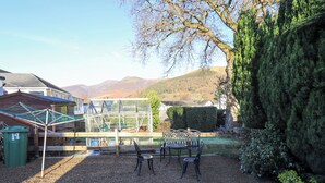 A backyard with a greenhouse, a metal table, and chairs. There is a green trash bin and a wooden fence. - Fairfell (Keswick)