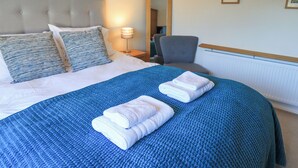 A neatly made bed with a blue quilt, two pillows, and two folded towels. - Fairfell (Keswick)