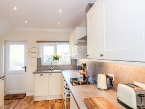 A compact kitchen with white cabinets, a wooden countertop, a toaster, a kettle, and a window with a view of the outside. - Glebe Cottage (Dumfries)