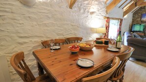 A wooden dining table with chairs, a bowl of fruit, a cheese board, and a wine bottle. - The Granary (Cardigan)