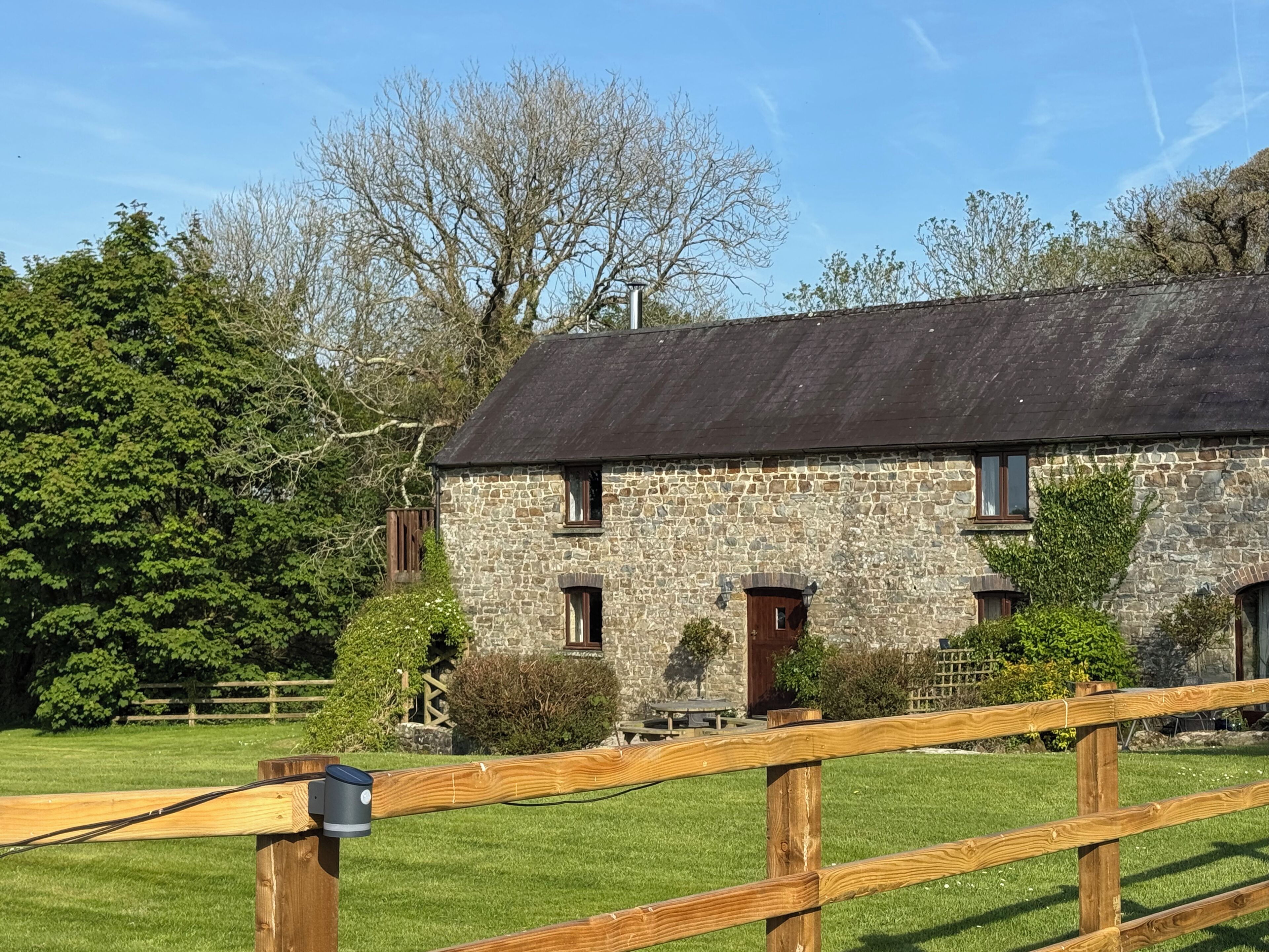 A stone building with a thatched roof, surrounded by a wooden fence and greenery.