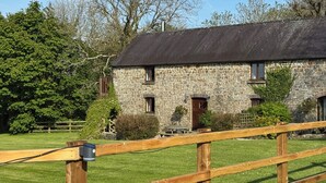 A stone building with a thatched roof, surrounded by a wooden fence and greenery. - The Granary (Cardigan)