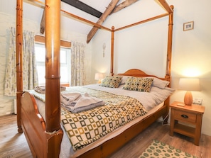 A four-poster bed with a wooden frame, a bedside table with a lamp, and a patterned bedspread.