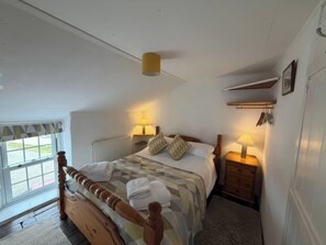 A bedroom with a wooden bed, two bedside tables with lamps, a window with a view, and a radiator. - Derlwyn (Newport)