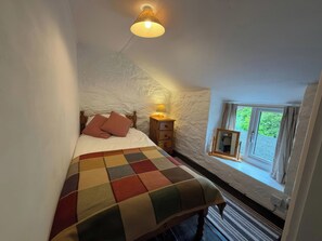A bedroom with a bed, a nightstand, a lamp, a window, and a mirror. - Derlwyn (Newport)