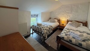A bedroom with two beds, a radiator, a window, and a lamp. - Derlwyn (Newport)