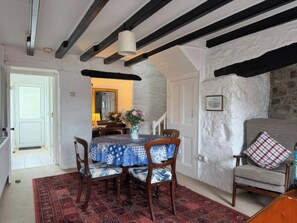 A dining area with a table set for four, a patterned rug, and a stone wall. - Derlwyn (Newport)