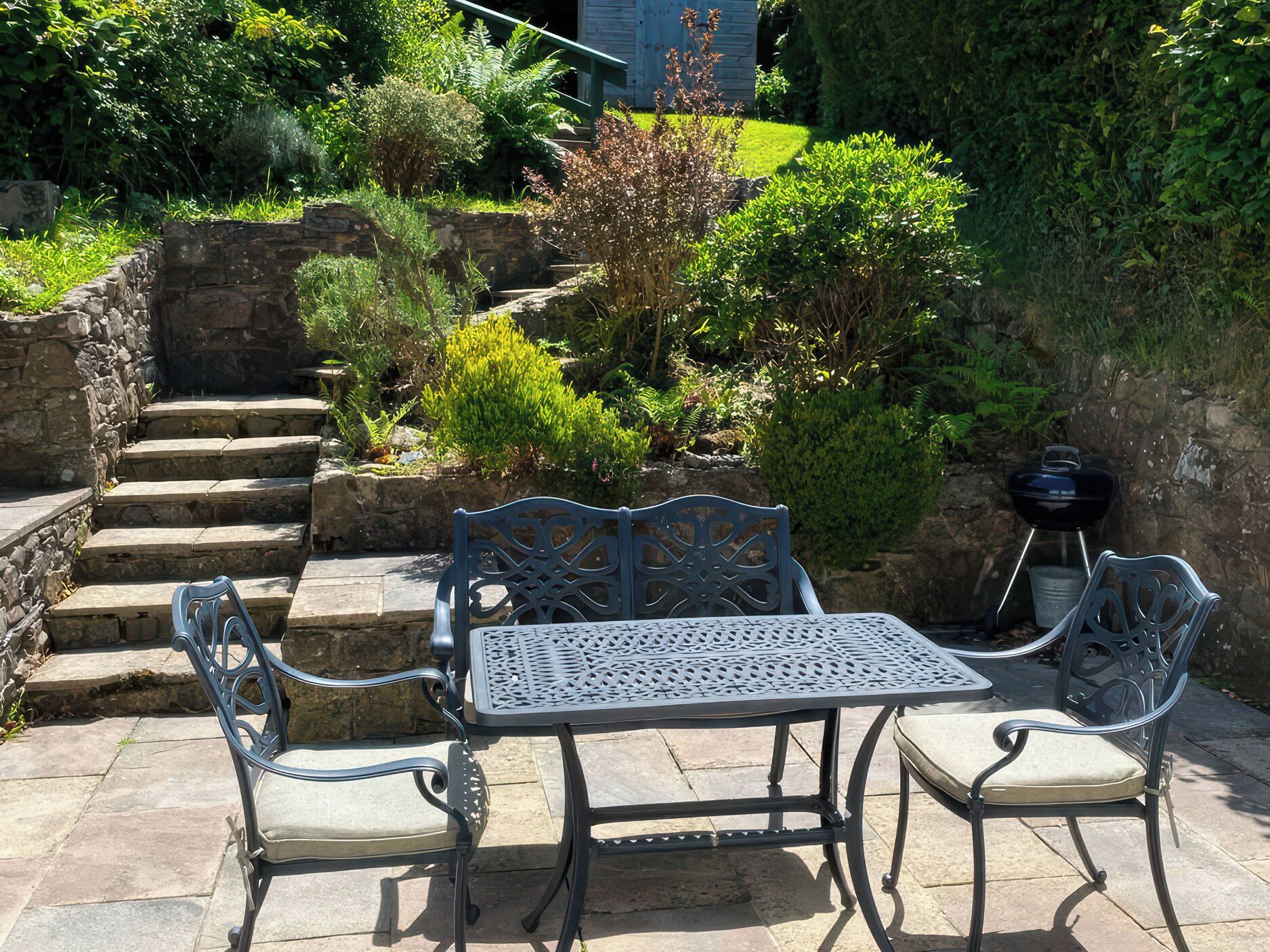 A patio with a metal table and chairs, stone steps, and a variety of plants.