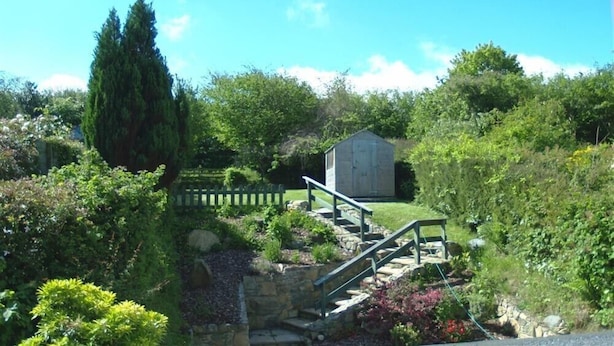 A garden with a wooden bench, a stone wall, and a shed. - Derlwyn (Newport)