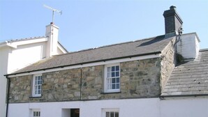 A two-story stone house with a white exterior, a chimney, and a door leading to the entrance. - Derlwyn (Newport)