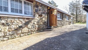A stone building with a wooden door, large windows, and a stone pathway leading to the entrance. - Otter Cottage (Newport)