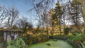 A rustic cabin surrounded by a pond and dense foliage. - Otter Cottage (Newport)