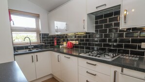 Una cocina moderna con armarios blancos, salpicadero de azulejos negros, electrodomésticos de acero inoxidable y una ventana con persianas.