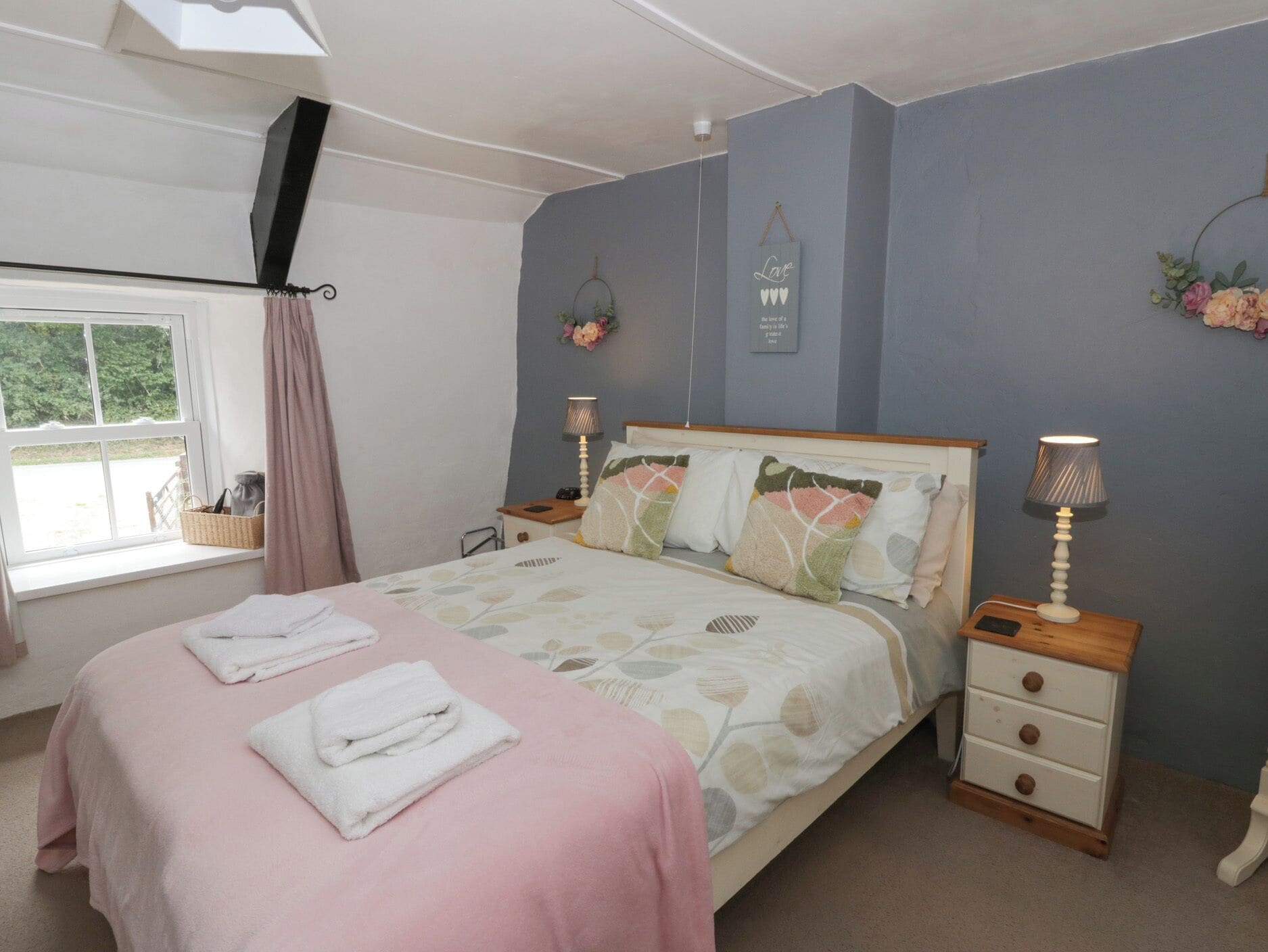 A bedroom with a bed, two bedside tables, a window with a curtain, and a wall with a decorative item.