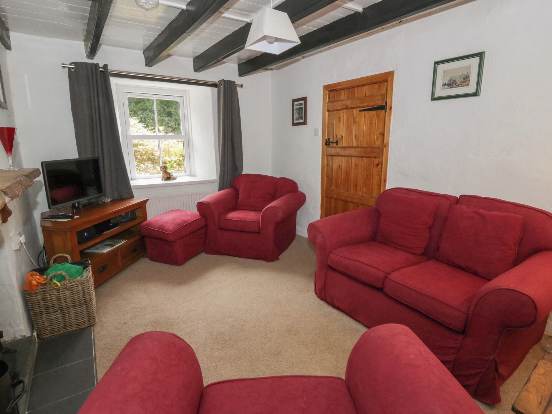 A living room with a television, red sofas, a wooden door, and a window with curtains.