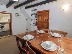 A dining area with a wooden table set for four, a washing machine, and a door with a sign. - Panteg, Cardigan (Cardigan)