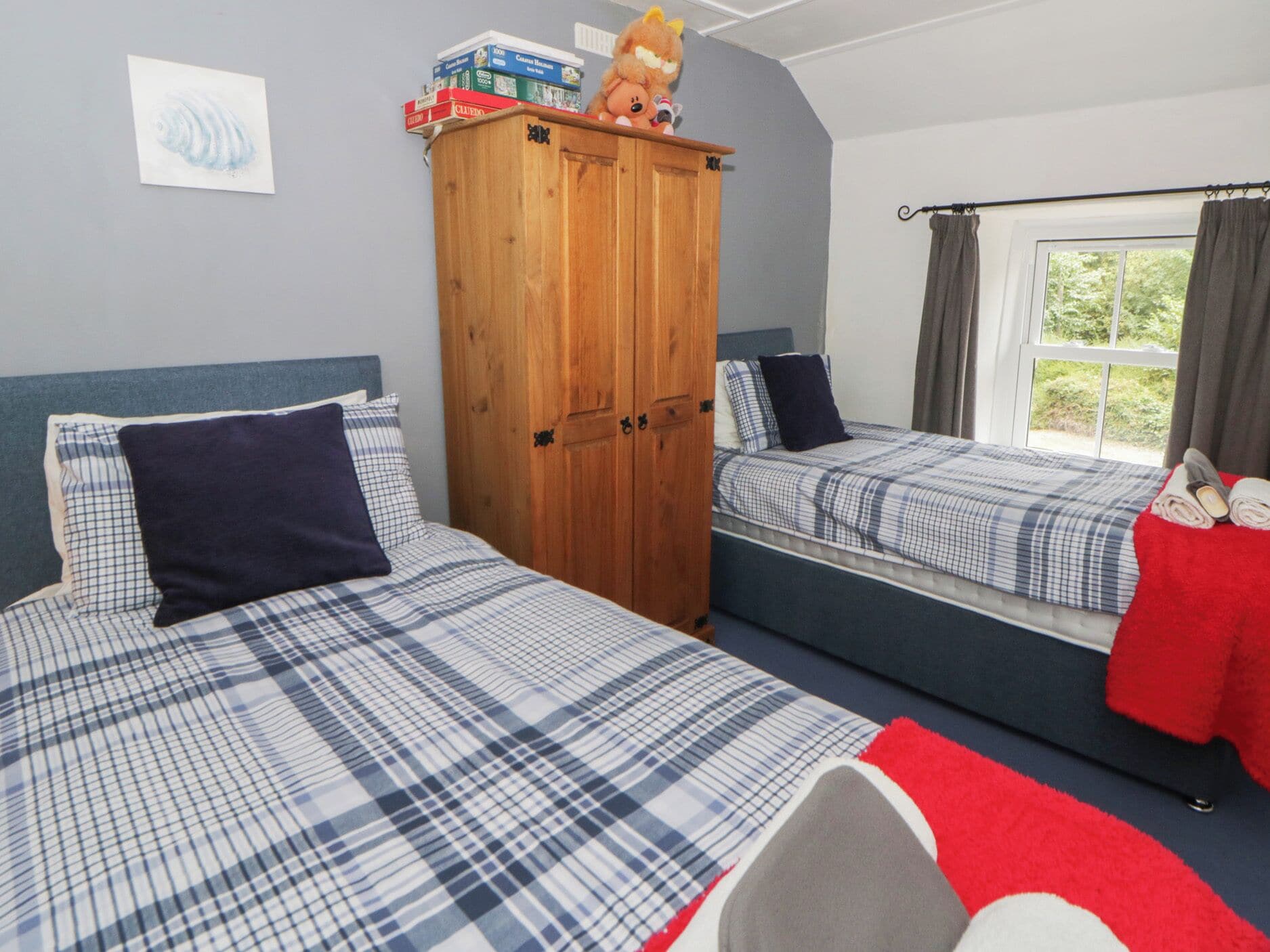 A bedroom with two beds, a wardrobe, and a window with curtains.