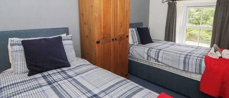 A bedroom with two beds, a wardrobe, and a window with curtains.