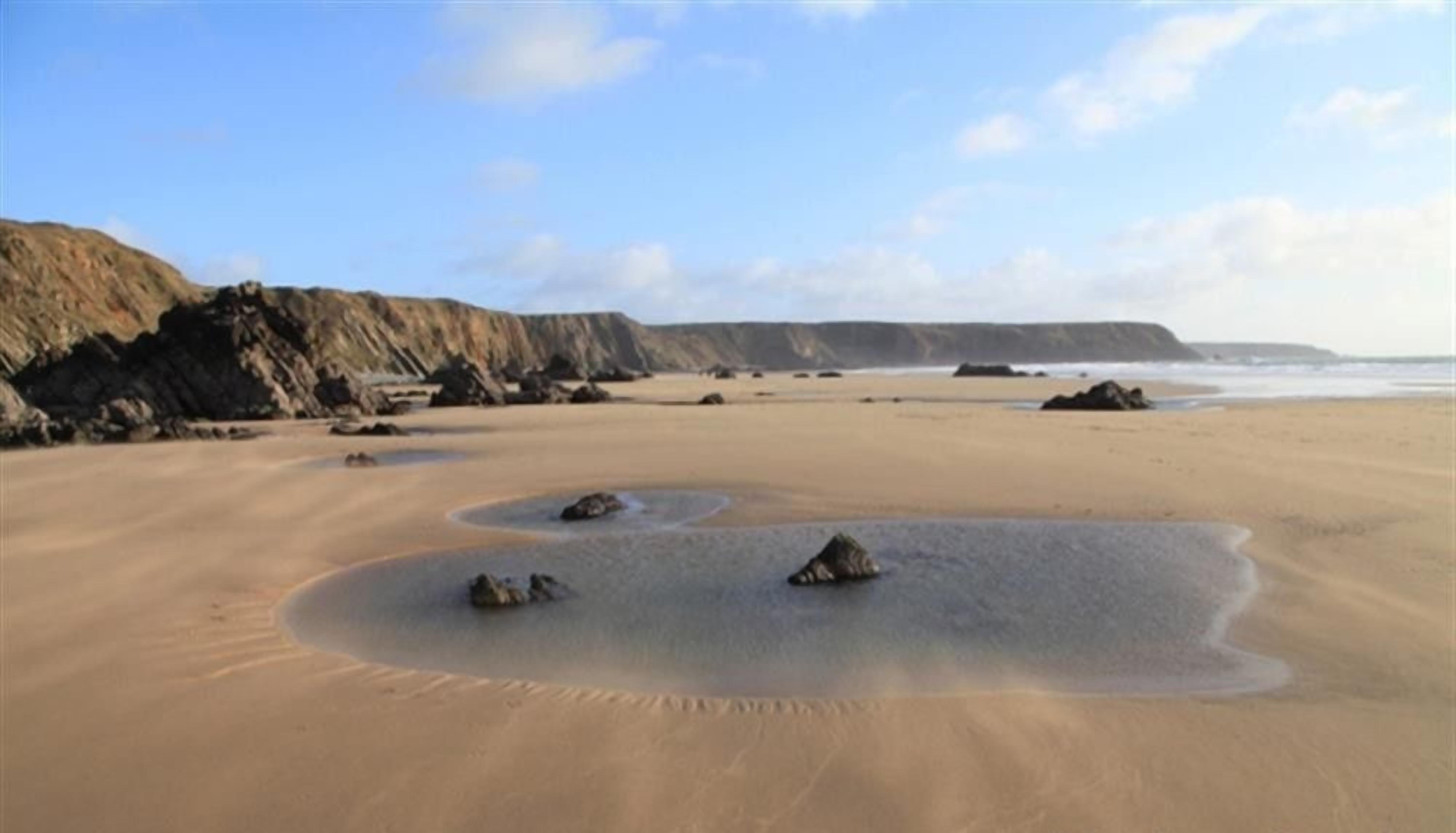 A sandy beach with rocks and cliffs in the background.