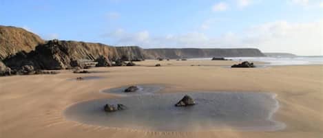 A sandy beach with rocks and cliffs in the background.