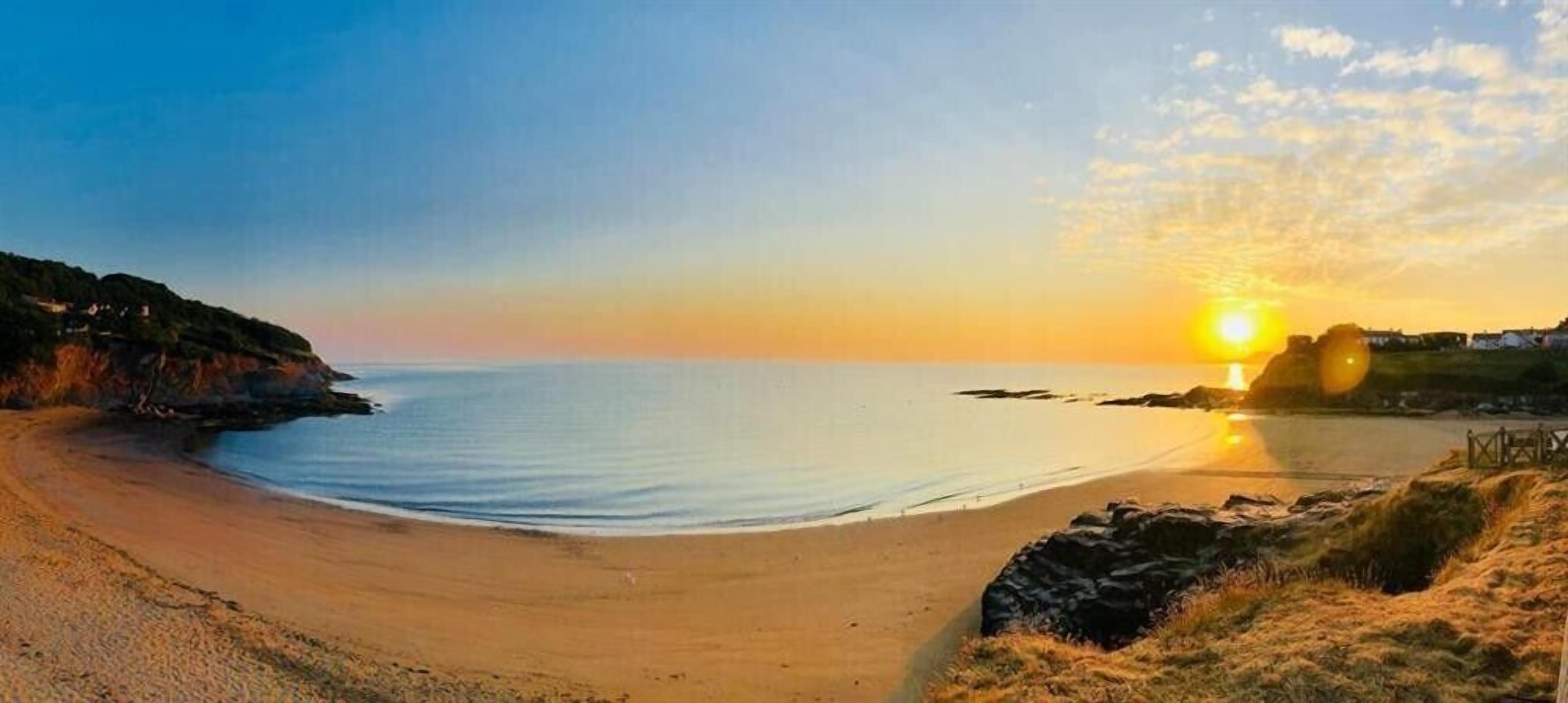 Een strand met een zonsondergang, kalm water en een rotsachtige kustlijn.