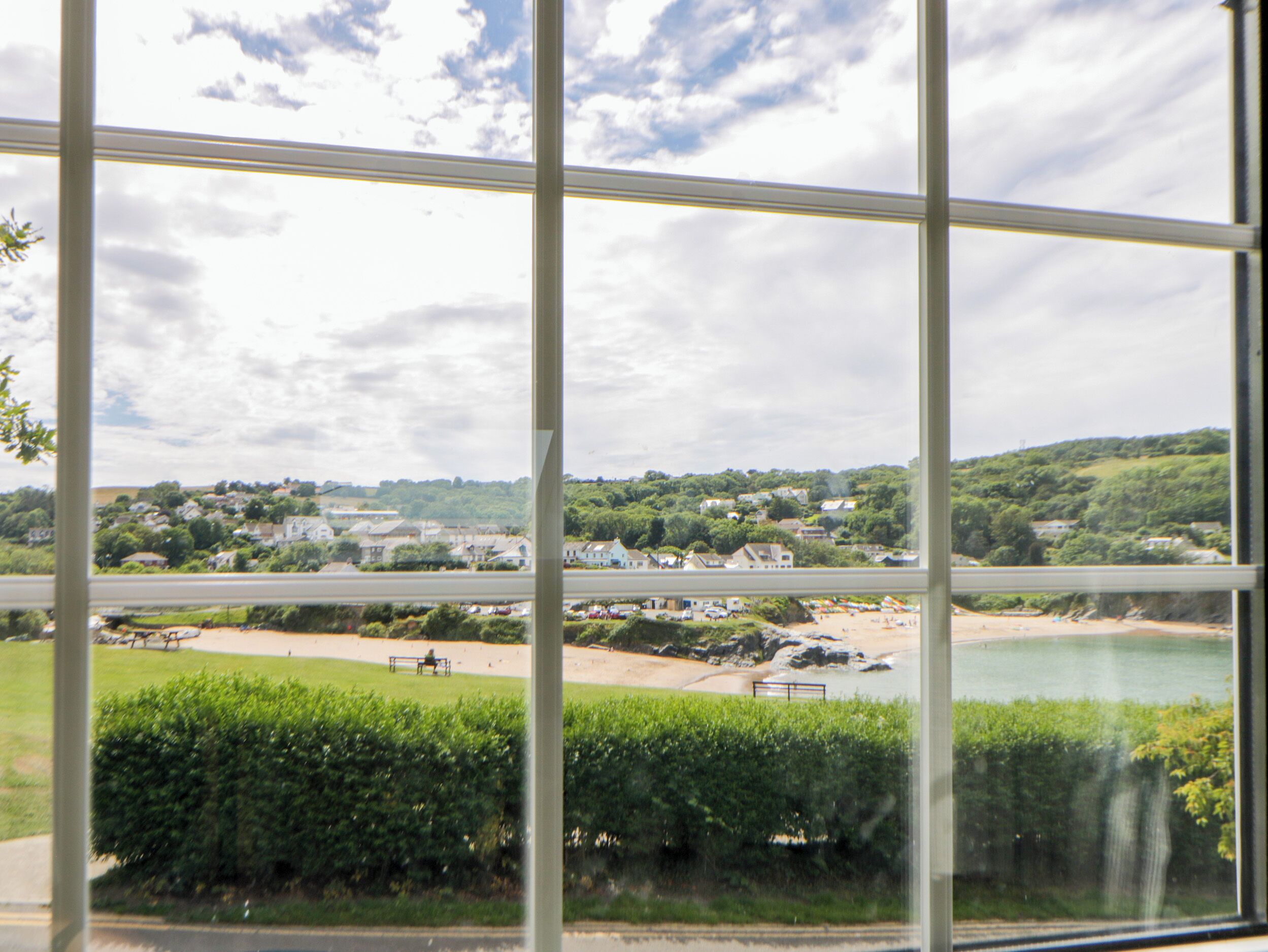 A view through a window with a clear sky, a green landscape, and a body of water.