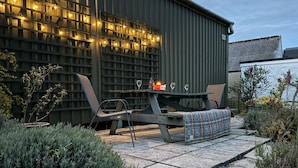 An outdoor patio with a table and chairs, a candle, and string lights. - The Farmhouse (Cardigan)
