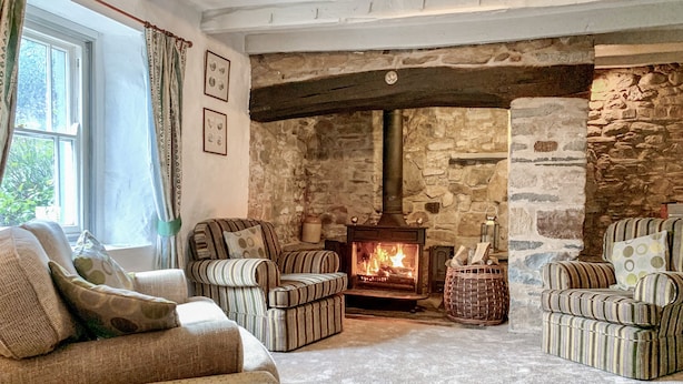 A cozy living room with a stone fireplace, striped armchairs, and a large window with curtains. - The Farmhouse (Cardigan)