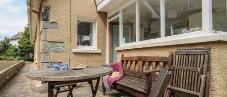A patio with a wooden table and benches, a stone wall, and a window with a view of the house.