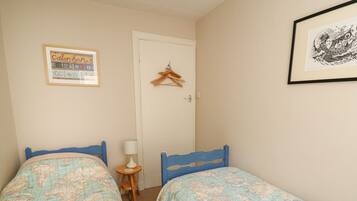 A bedroom with two beds, a small table with a lamp, a door with a hanger, and a framed picture on the wall.