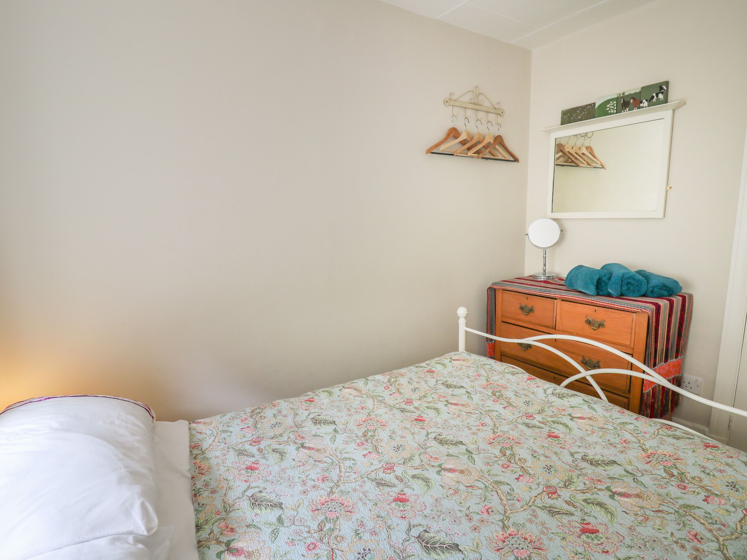 A bedroom with a bed, a dresser, a mirror, and a wall-mounted coat rack.