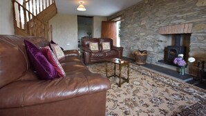 A cozy living room with a stone wall, a fireplace, a leather sofa, and a staircase. - Panteurig Farmhouse (Goodwick)