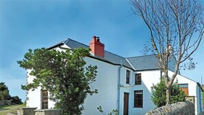 A white house with a stone wall, a red chimney, and a tree in front. - Panteurig Farmhouse (Goodwick)