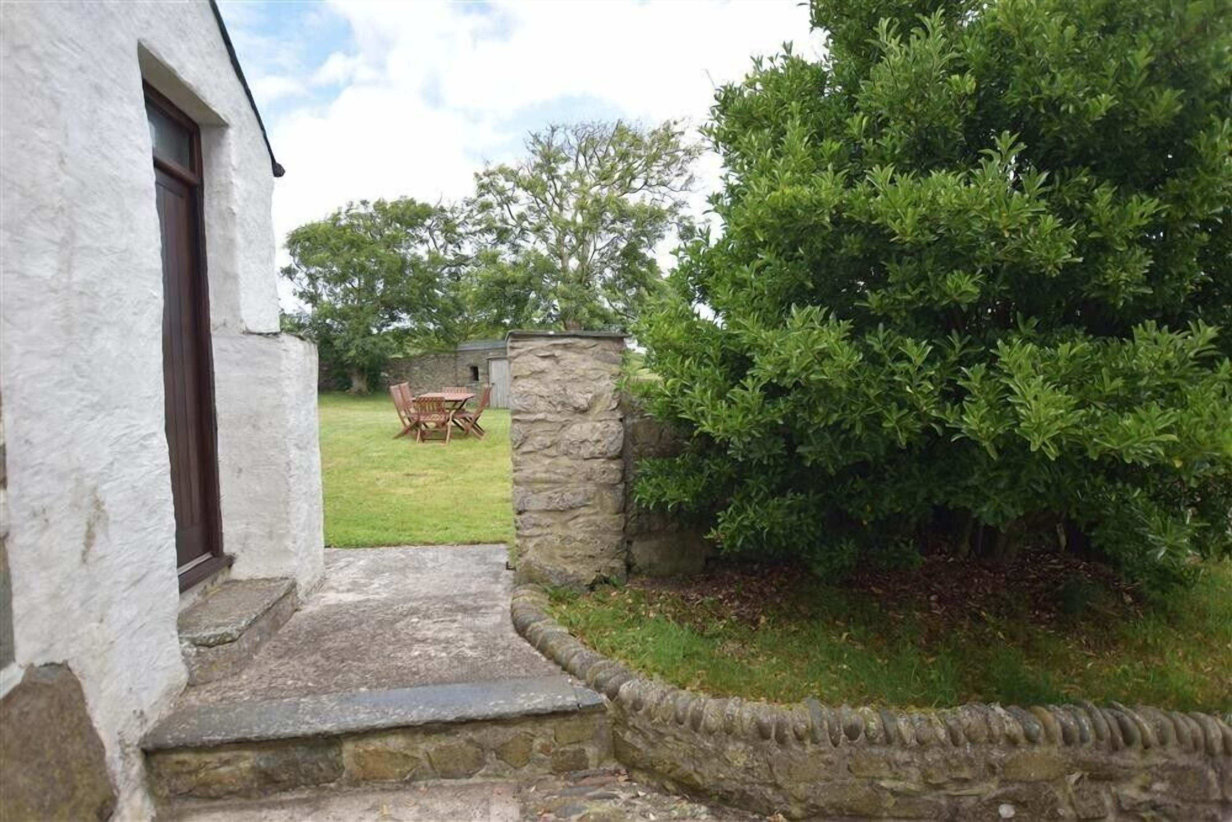A stone pathway leading to a grassy area with a stone wall and a small table and chairs.