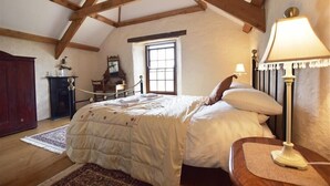 A bedroom with a bed, a nightstand, a lamp, a window, and wooden beams on the ceiling. - Panteurig Farmhouse (Goodwick)