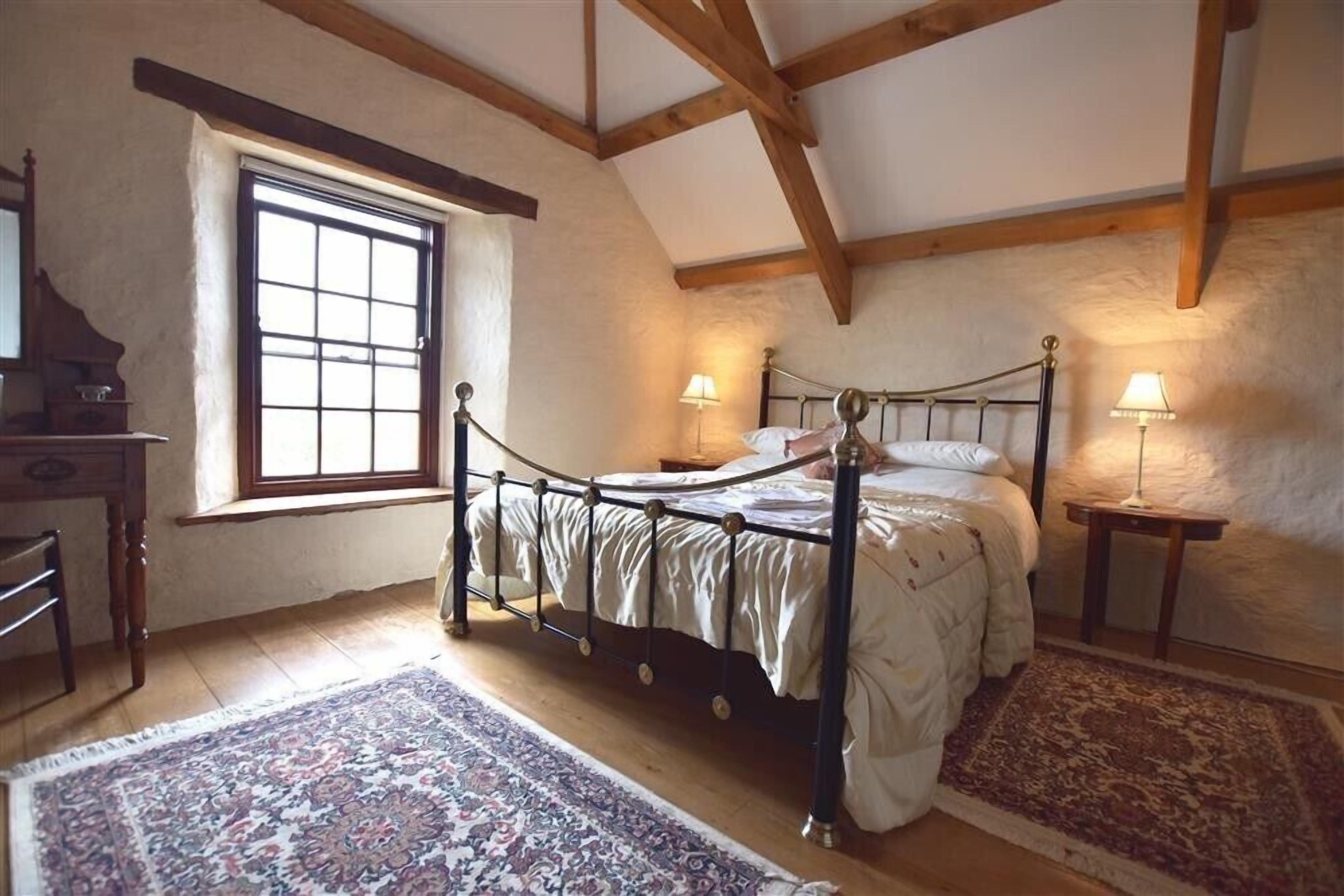 Un dormitorio con cama con dosel, vigas de madera, una ventana y dos lámparas de noche.