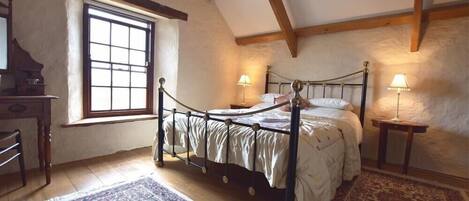 A bedroom with a four-poster bed, wooden beams, a window, and two bedside lamps.