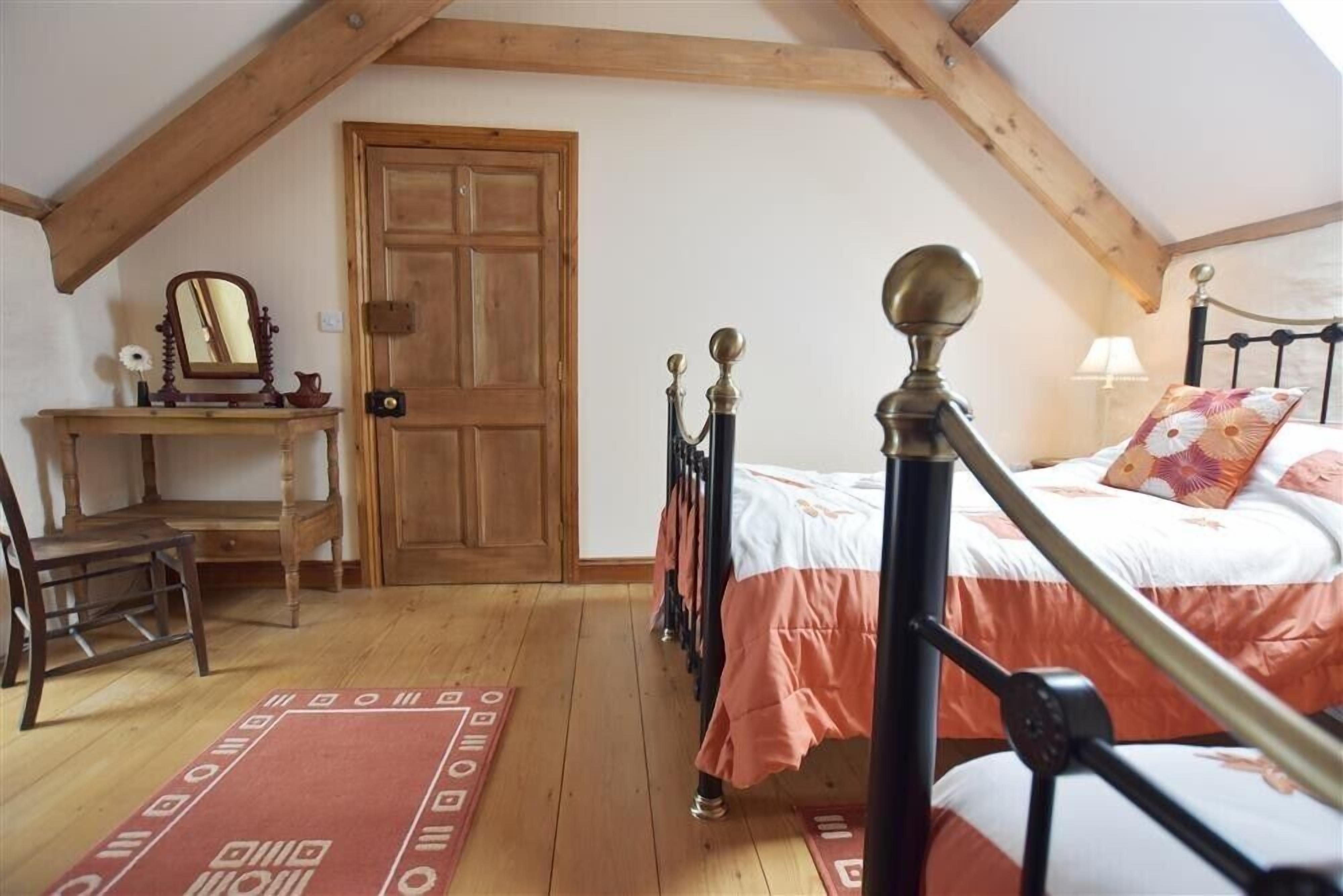 Une chambre avec une porte en bois, un lit avec un cadre noir, un tapis rouge et blanc, et un bureau avec un miroir.
