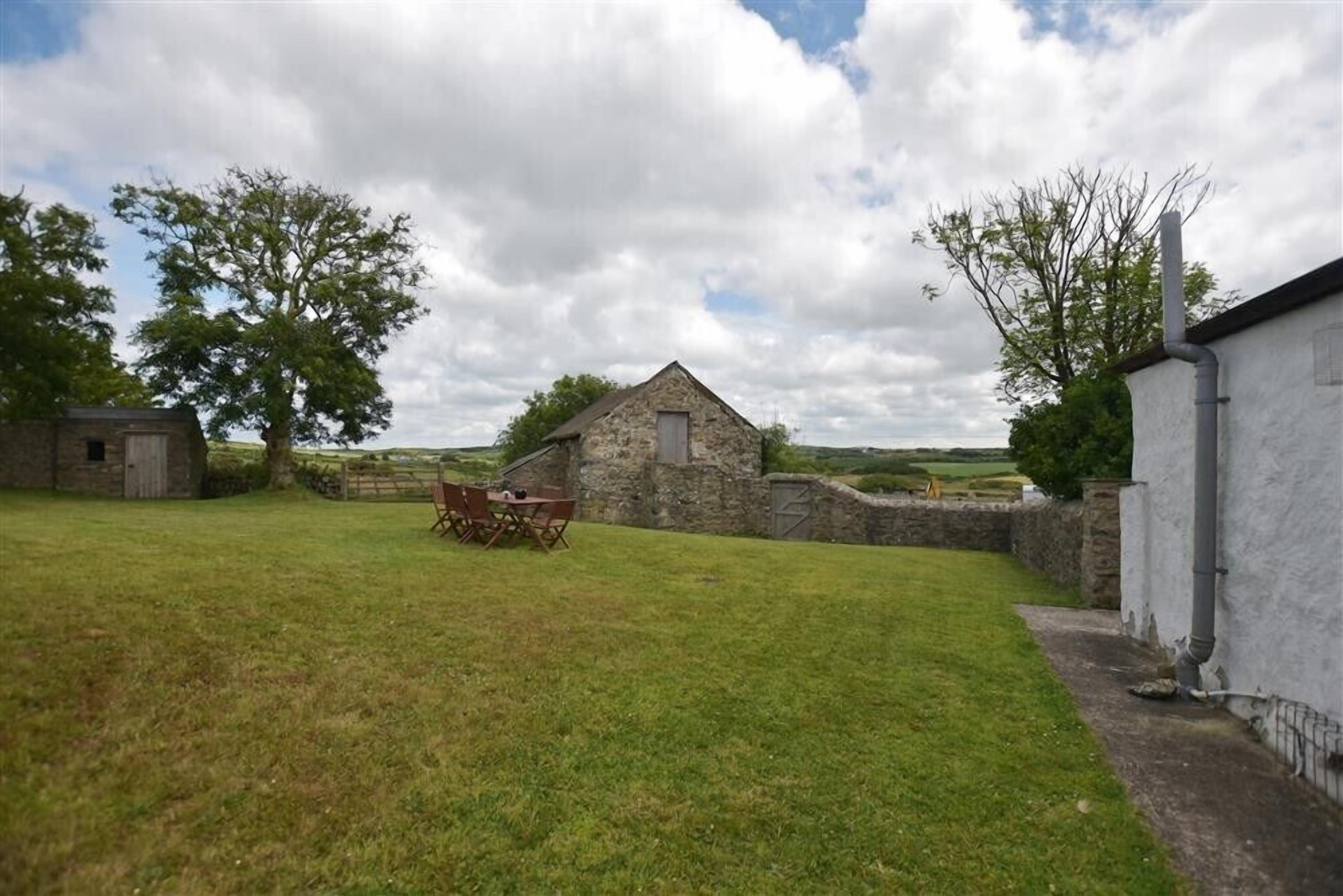 A stone building with a small attached shed, surrounded by a grassy yard and trees.