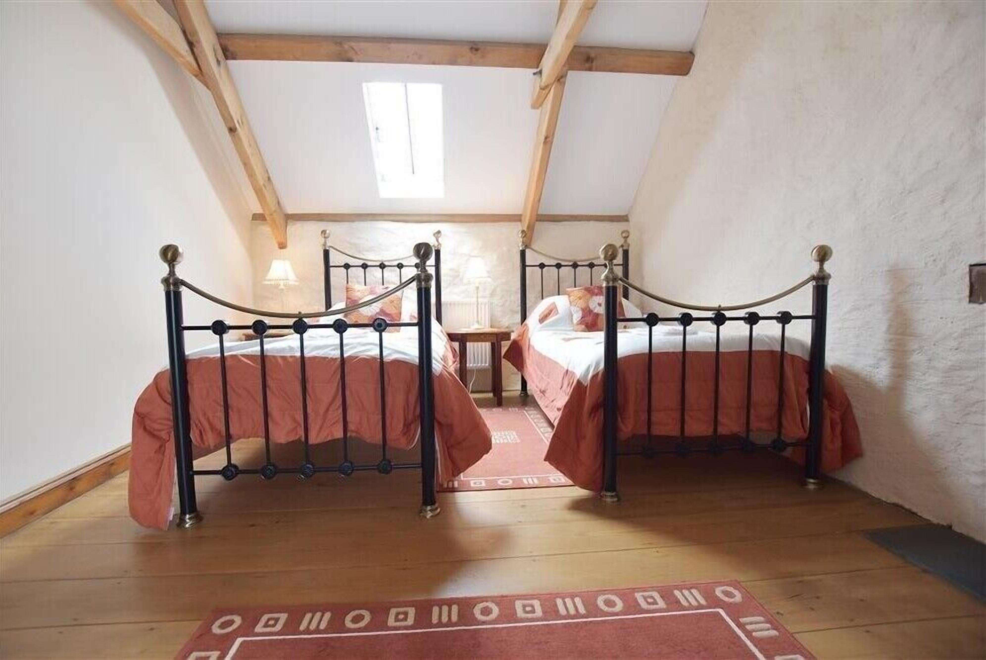 Una habitación con dos camas, vigas de madera, techo inclinado y una ventana.