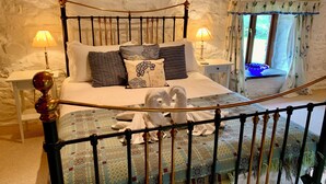 A bedroom with a stone wall, a bed with patterned bedding, two bedside lamps, and a window with curtains.