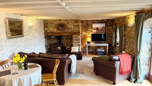 A cozy living room with stone walls, a fireplace, a television, and leather furniture.