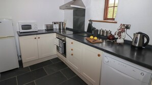 A compact kitchen with white cabinets, a microwave, toaster, kettle, and a dishwasher. - Panteurig Cottage (Goodwick)