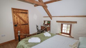 A room with a bed, a wooden door, a small table with a mirror, and a window. - Panteurig Cottage (Goodwick)