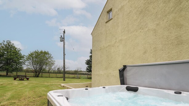 Un jacuzzi con muelle de madera, mesa de picnic y zona verde con árboles y cerca.